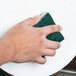 A hand using a green Scrubble tough-scour sponge to clean a white sink.