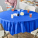 A woman pouring orange liquid into a glass on a table with a blue Creative Converting OctyRound tablecloth.