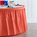 A coral orange plastic table skirt on a table with cupcakes.