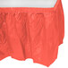 A coral orange plastic table skirt with ruffled edges.