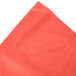 A coral orange plastic table skirt in packaging with a coral orange background.