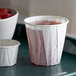 A white Genpak paper souffle cup filled with liquid on a tray with a bowl of strawberries.