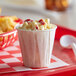 A white Genpak paper souffle cup filled with macaroni and cheese on a red tray.