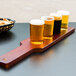 A row of Libbey Straight Sided Tasting Glasses filled with beer on a wooden flight paddle.