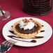 A chocolate tart with whipped cream and chocolate sauce on a 10 Strawberry Street white bone china plate.