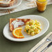 An Acopa ivory stoneware platter with scrambled eggs, toast, and orange slices.