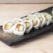 A rectangular stoneware slab with sushi rolls on a wood surface.
