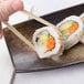 A hand holding chopsticks to a sushi roll.