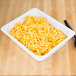 A white Thunder Group melamine food pan filled with macaroni and cheese on a wooden surface.