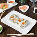 A plate of sushi on a 10 Strawberry Street white rectangular porcelain platter with chopsticks on a table.