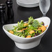 A white porcelain oval bowl filled with salad on a table.