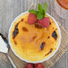 A white porcelain fluted creme brulee dish filled with creme brulee topped with raspberries and mint.