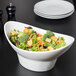 A white porcelain oval bowl filled with salad and vegetables on a table.