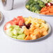 A Durable Packaging round foil catering tray with a plate of fruit and vegetables on a table.