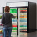 A woman standing in front of a Beverage-Air glass door refrigerator filled with drinks.