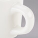 A close up of a Tuxton eggshell white china cup with a handle.