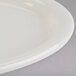 A close up of a Tuxton Nevada oval white china platter with a curved edge on a gray surface.