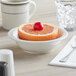 A Tuxton Nevada eggshell narrow rim china bowl filled with grapefruit on a table with a cup of tea.