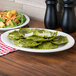A Tuxton eggshell white china platter with green ravioli and salad on it.