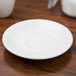 A Tuxton Reno white china saucer on a wood surface.