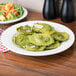 A Tuxton Reno ivory china plate with green ravioli on a wooden table.
