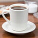 A Tuxton white Tiara mug on a saucer with coffee.