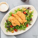 An oval EcoChoice palm leaf tray with fried chicken and salad on it.