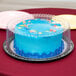 A blue cake in a D&W Fine Pack cake display container with a clear dome lid on a table in a bakery display.