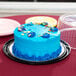A blue cake on a plate with a clear plastic dome lid.