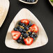 A TreeVive triangular palm leaf plate with strawberries and blueberries.