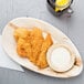 An EcoChoice oval palm leaf tray with fried chicken and dipping sauce.