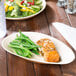 A TreeVive by EcoChoice oval palm leaf tray with a salad and green beans on a table.