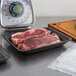 A black CKF foam meat tray holding raw steaks on a counter.