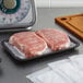 A black foam CKF meat tray with a piece of meat on it on a counter.
