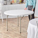 A man standing next to a Lancaster Table & Seating 48" round folding table with a white surface.
