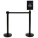 A black sign with white text on a Lancaster Table & Seating crowd control stanchion.