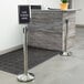 A Lancaster Table & Seating crowd control stanchion with a sign on a counter.