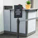 A Lancaster Table & Seating stanchion sign frame holding a "Line Forms Here" sign with a clear cover.