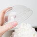 A hand holding a Solo clear plastic dome lid over whipped cream on a clear plastic container.