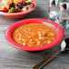 A GET Diamond Harvest cranberry melamine bowl of soup and a bowl of salad on a table in a family-style restaurant.