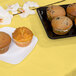 A plate of muffins on a yellow table with a Creative Converting Mimosa Yellow table cover.