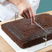 A person using a Wilton wire cake leveler to cut a chocolate cake.