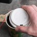 A hand holding a white plastic lid on a coffee cup.