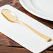 A Fineline gold plastic spoon on a napkin next to a plate.