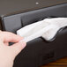 A hand pulling a tissue paper out of a black Vollrath napkin dispenser.