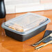 A Genpak clear plastic rectangular lid on a plastic container with food inside next to a fork.
