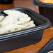 A black Genpak Smart-Set Pro rectangular microwaveable container filled with pasta and sauce on a table.