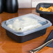 A black Genpak rectangular plastic container with food in it on a table.