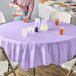 A table with a Creative Converting Luscious Lavender Purple tablecloth and glasses of juice.