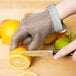 A person wearing a San Jamar stainless steel mesh glove cuts a lemon.